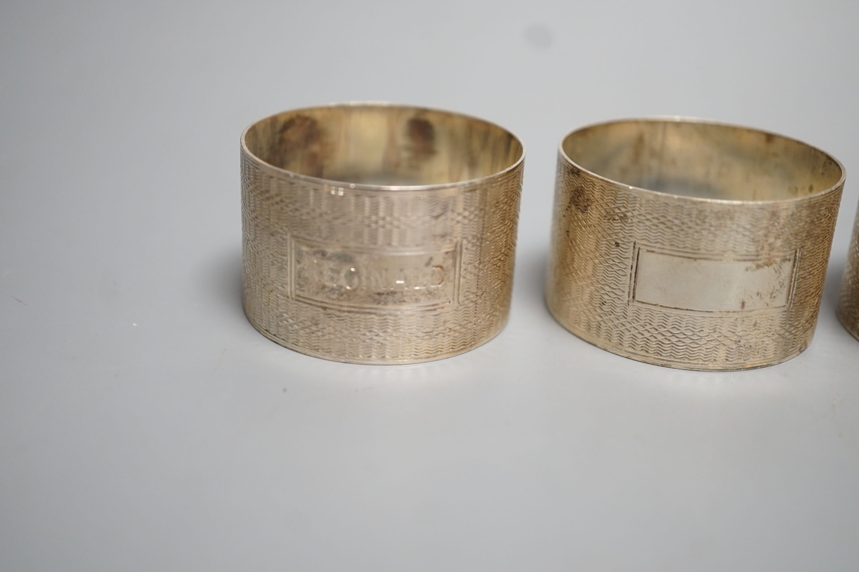 A set of four George VI engine turned silver napkin rings, H. Bros, Birmingham, 1943/4, two engraved with names.